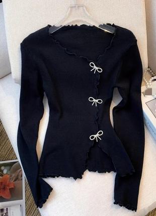 Черный свитер с бантиками и волнистым краем.