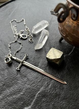 Підвіска меч на ланцюжку срібного кольору.