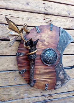 Кованый настенный бра ручной работы на фоне спартанского щита с драконом