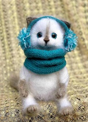 Белая пушистая зимняя кошечка в наушниках и снуде