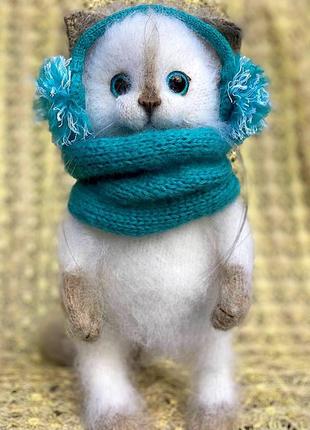 Белая пушистая зимняя кошечка в наушниках и снуде