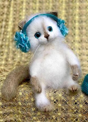 Белая пушистая зимняя кошечка в наушниках и снуде