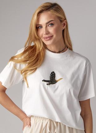 Женская футболка украшена птицей из страз.