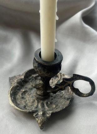 Бронзовий свічник з ручкою та візерунками, що від часу вже почали стиратися.