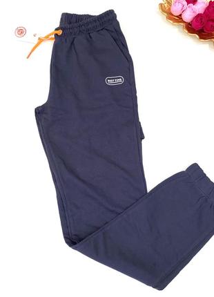 Спортивные штаны трехнить темно синего цвета с оранжевыми шнурками на поясе. пояс регулируется.