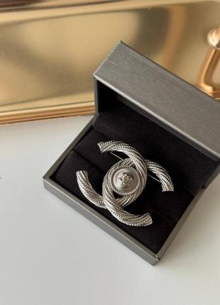 Брендова брошка в срібному кольорі у вигляді логотипу