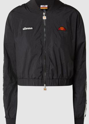 Блузон от ellesse изготовлен из прочного материала и имеет укороченный крой. он имеет спущенные плечи, контрастные полосы и логотипы.