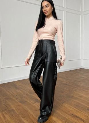 Актуальная модель брюк из эко-кожи на байке: высокая посадка, широкий крой, акцентные накладные карманы.