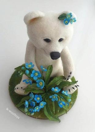 Полярный мишка в бело-бежевом цвете сидит на полянке с сине-голубыми цветами2 фото