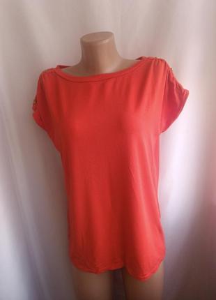 Футболка декорована гудзиками на плечах.