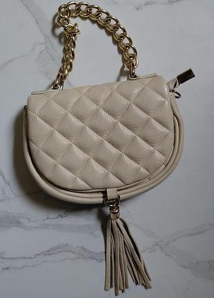 Стильна жіноча шкіряна сумка-клатч бежевого кольору з золотим ланцюжком і китицею.
