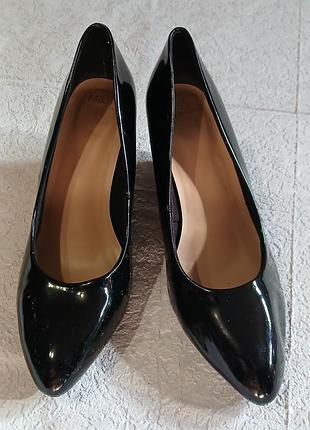 Женские туфли лодочки на танкетке черного цвета из искусственной лакированной кожи.