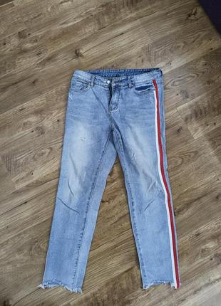 Джинсы женские с легкими потертостями, с боковой стороны украшены контрастной полосатой вставкой в красном и белом цветах