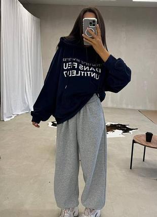 Зручний жіночий повсякденний костюм з тринитки на флісі оверсайз худі зі шнурком та написом спереду з кишенею кенгуру та штани вільного крою