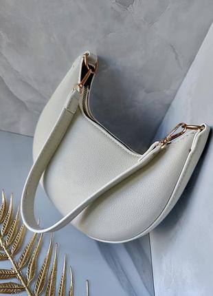 Женская сумка-полумесяц (также известная как сумка-хоб или багет) с золотистой фурнитурой молочного цвета