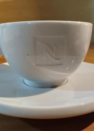На картинке – белые фарфоровые чашки для кофе с блюдцем, принадлежащим к бренду nespresso.