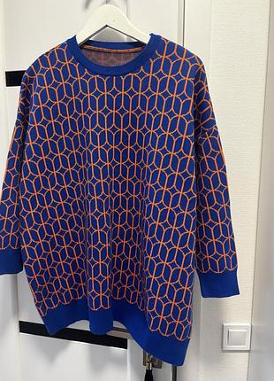 Синій светр з помаранчевим геометричним візерунком.