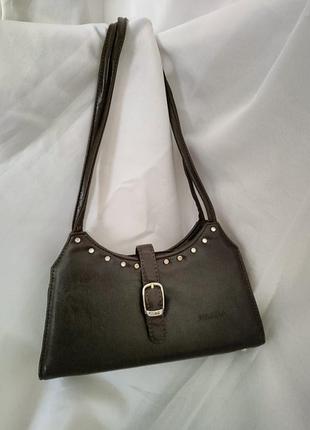 Небольшая плечевая сумка темного цвета с пряжкой и декоративными серебристыми заклепками.