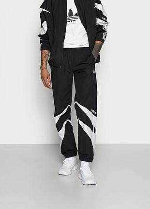 Чорні спортивні штани adidas з білими графічними вставками та трьома смужками вздовж штанин.