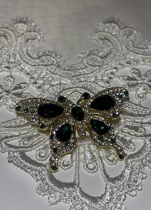 Брошка золотого кольору з зеленими камінцями