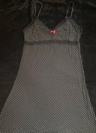 Це чорна нічна сорочка в білий горошок з тонкими бретельками, мереживною обробкою та маленьким червоним бантом.