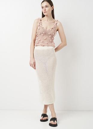 В'язаний гачком топ кольору слонової кістки з ажурною сітчастою структурою та прикріпленими квітковими аплікаціями.