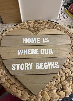 Дерев'яна декоративна табличка у формі серця з написом "home is where our story begins".