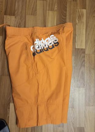 Мужские спортивные шорты оранжевого цвета с большим логотипом бренда adidas.