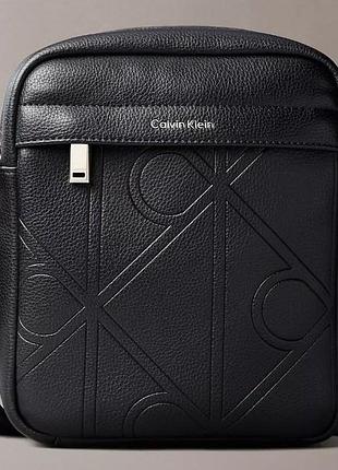 Чоловіча сумка через плече від бренду calvin klein, модель emblem aop emboss reporter у чорному кольорі
