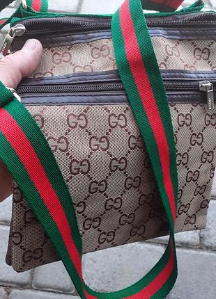 Сумка в стиле gucci представляет собой бежевый мессенджер с коричневым логотипом gg и характерным зеленым-красным ремешком.реплика.р-ры 22,5*20*4см.