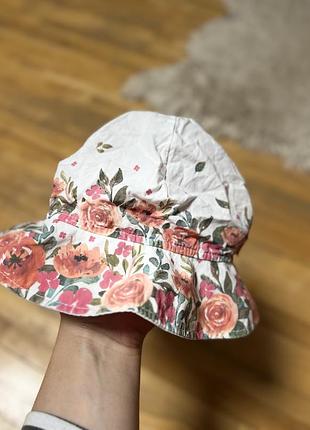 Дитяча панама marika “floral bucket hat” — біла з квітковим принтом у рожево‑персикових тонах. виконана з бавовни, легка й дихаюча.