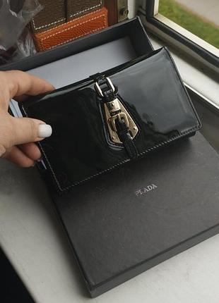 Черный женский лакированный кошелек-континенталь бренда prada.
