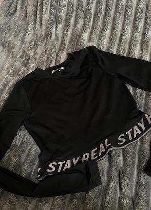 Чорний кроп-топ із довгими рукавами та написом "stay real" на еластичному поясі