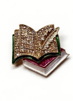 Брошь - кулон в виде открытой книги с пером выполнена из металла золотистого цвета с инкрустацией кристаллами и эмалью.