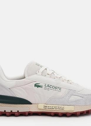 Білі кросівки lacoste elite active мають замшеві вставки та унікальний текст із координатами на бічній стороні