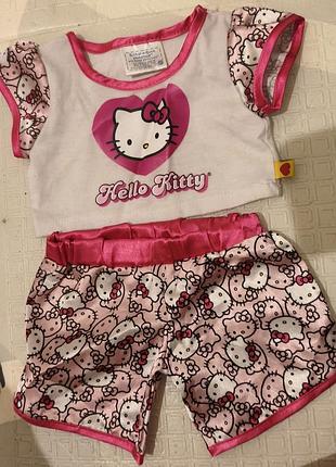 Комплект одежды от build-a-bear workshop включает в себя белую футболку с принтом hello kitty и атласные шорты с розовым рисунком.