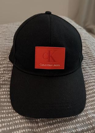 Чорна бейсболка calvin klein jeans виділяється контрастним червоним патчем із тисненим логотипом