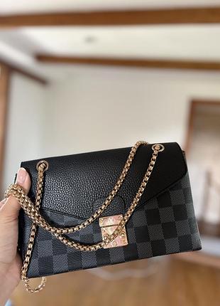 Жіноча сумка louis vuitton pallas chain виконана в чорній канві damier graphite з чорним шкіряним клапаном та золотистою ланцюговою ручкою.
