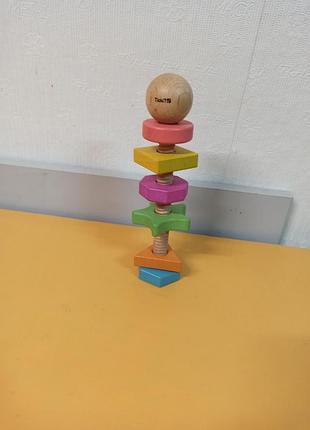 Розвиваюча іграшка — tickit rainbow wooden shape twister, що складається з великого дерев'яного болта та різнокольорових геометричних фігур.