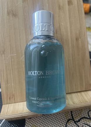 Гель-санітайзер для рук molton brown coastal cypress & sea fennel у прозорому синьому флаконі.