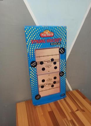 Настольная игра «string hockey» (string puck) от бренда play world, представляющей собой деревянную доску с резинками для опрокидывания шайб.