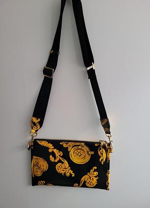 Сумка versace jeans couture имеет черный цвет с золотистым барочным принтом.