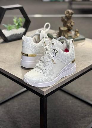 Білі кросівки michael michael kors моделі georgie trainer, які вирізняються золотистою вставкою на п'яті.