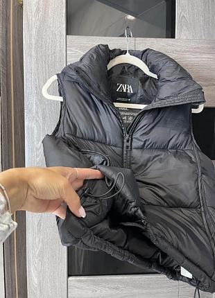 Чорний дутий жилет бренду zara має матовий водовідштовхувальний матеріал та незнімний капюшон.