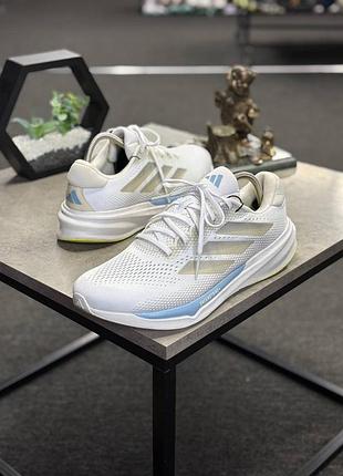Кросівки для бігу adidas supernova stride 2. це бігове взуття в білому кольорі з металевими сріблястими вставками та блакитними акцентами.