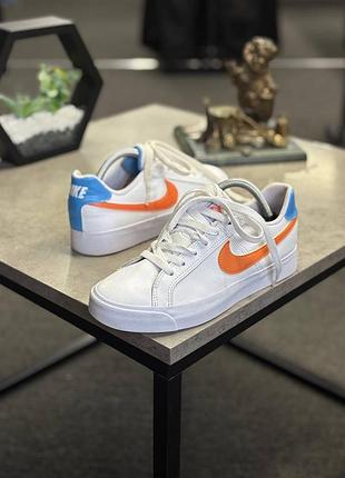 Жіночі кросівки nike court royale ac, які виділяються яскравими помаранчевими логотипами swoosh та блакитними акцентами на п'яті.