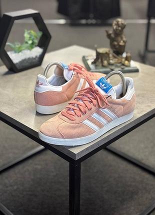 Замшеві кросівки adidas gazelle у персиково-рожевому кольорі, що відрізняються контрастними білими фірмовими смужками.