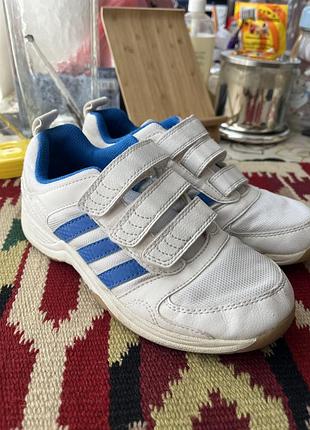 Дитячі кросівки adidas білого кольору мають сині фірмові смужки та зручні застібки-липучки