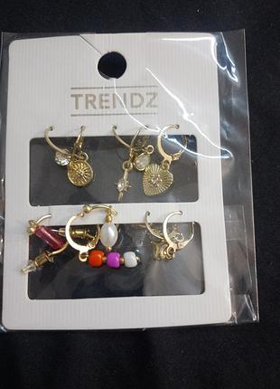 5 наборов серег бренда trendz включает несколько пар с золотистым покрытием и разнообразными подвесками, такими как сердца и солнце.