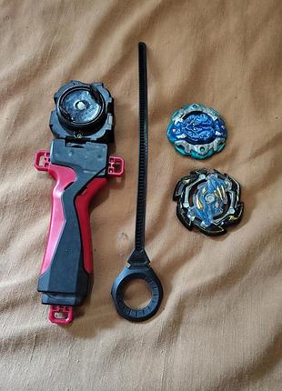 Набор игрушек beyblade burst, включающий пусковое устройство (лаунчер) с ручкой и два волчка.